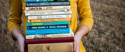 pile of books held by somebody in a yellow jumper