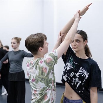 A dancer raising her right arm with more dancers in the background