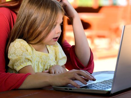 Child sat at laptop with mother