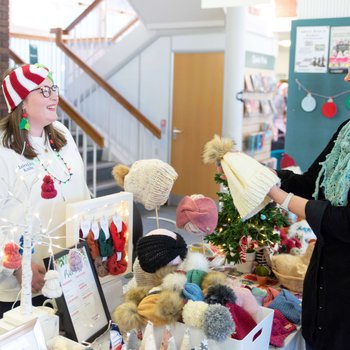 Stallholder wearing a knitted santa hat smiles while a customer holds one of their hats, smiling