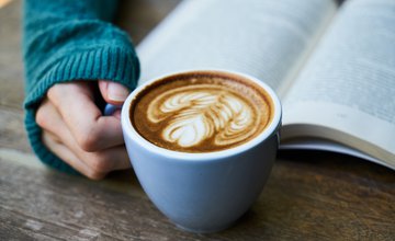 a cup of coffee with latte art next to an open book