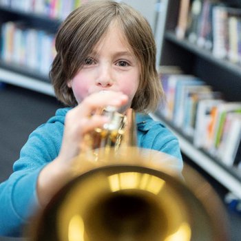 A close up of a child wearing a blue top playing a brass instrument.
