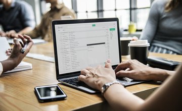 Hands typing on a computer keyboard with a screen on a table