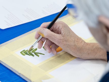 An older person's hands painting a leaf.