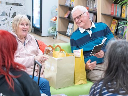 Older adults enjoying a reading group session, sat on comfortable chairs chatting