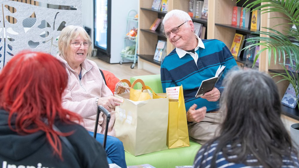 Older adults enjoying a reading group session, sat on comfortable chairs chatting