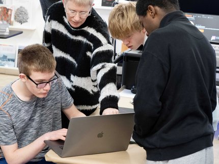 An image of 4 people gathered around a laptop in an art studio.