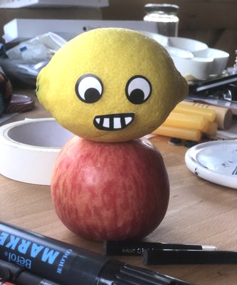 Lemon with stick on eyes and mouth, balanced on apple.