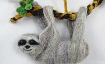 A sloth made out of felt hanging on a pipe cleaner branch