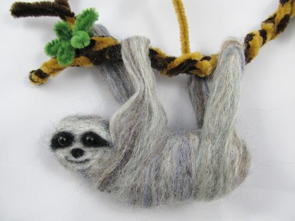 A sloth made out of felt hanging on a pipe cleaner branch
