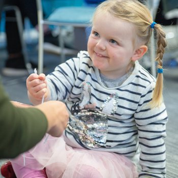 Child looking up smiling at adult, making a friendship bracelet