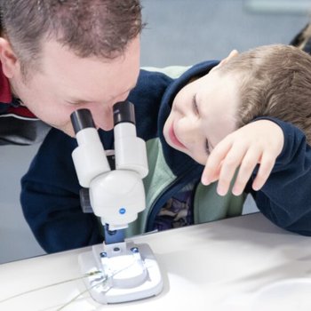Man looking through a microscope with child looking at him, smiling