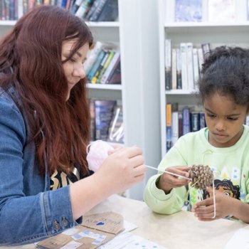 Woman and girl doing a craft activity using wool and pine cones
