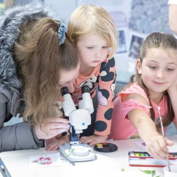 Women looking through a microscope with 2 young girls painting