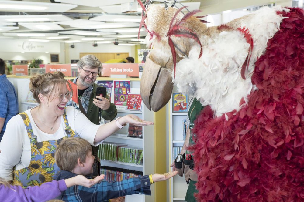 Library staff and children both feeding a bird puppet of white and red colour.