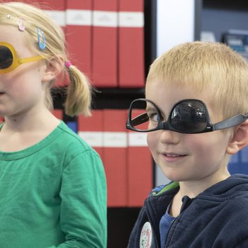 children with sunglasses on, upside down with one lens removed, smiling