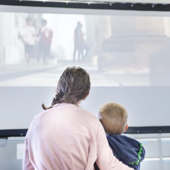 parent and child in embrace, watching a film on a large projector screen