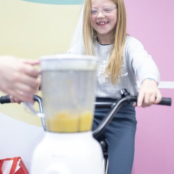 Child riding an exercise bike, connected to a blender making a smoothie