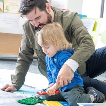 A man and young boy sitting together doing a floor-based printing activity