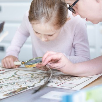 A young girl looking at a map using a magnifying glass