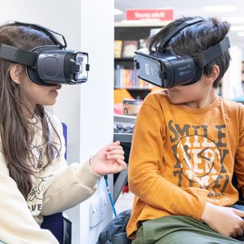 A girl and a boy seated and wearing virtual reality headsets