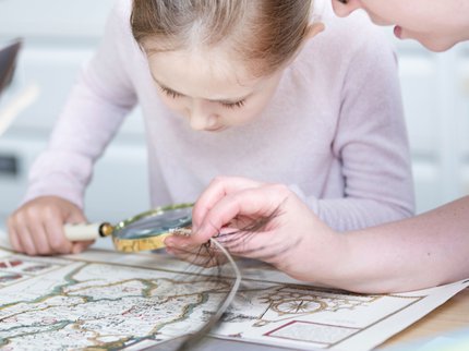 Child and an adult studying a historical map with a magnifying glass