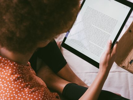 woman sat cross legged reading an ebook on a tablet