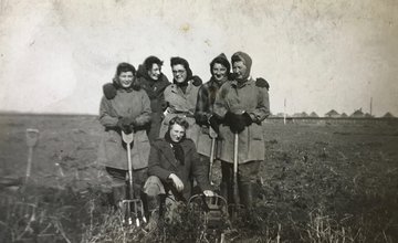 A black and white image of women standing in a field with tools during world war two