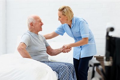 image of female healthcare worker dressed in blue helping elderly patient out of bed