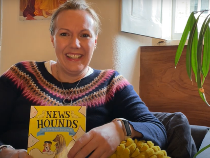 An author sits on a sofa with her book called News Hounds
