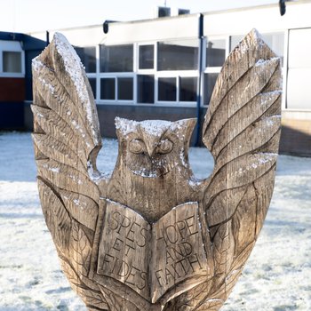 Front of the Oak owl sculpture, an owl with open wings and a book with the school motto in Latin