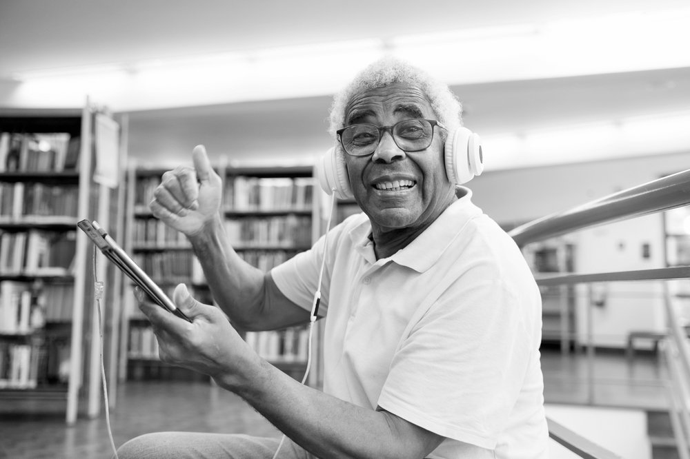 Photograph of a man listening to an e-audiobook with headphones, while in a library