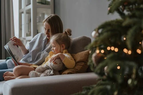Woman and girl reading by Christmas tree