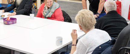 Group of people sat around a table drinking tea and coffee, at a library Places of Welcome group