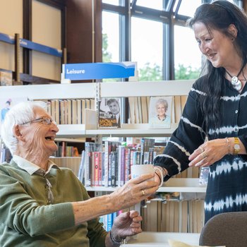 Elderly gentleman and volunteer shaking hands in a library setting