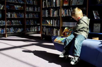 A young boy wearing blue jeans reads a book at the library