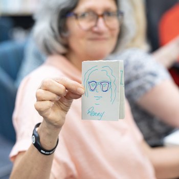 A woman at a workshop, holding out a piece of paper with her leaf drawing