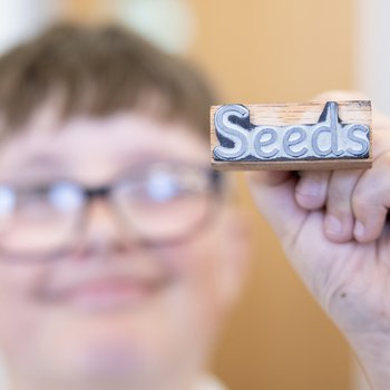 Boy wearing glasses, holding up a stamp that says seed.