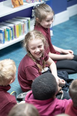 A group of children sat on the floor in Warsop Library, smiling, surrounded by book shelves