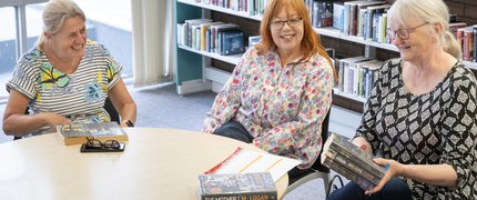 Three book club members are gathered around a table discussing books.