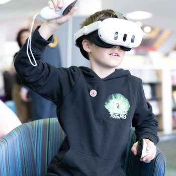 Child wearing a VR headset and holding controllers, with his hands in the air