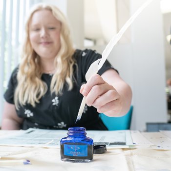 Person dipping a quill in ink and smiling