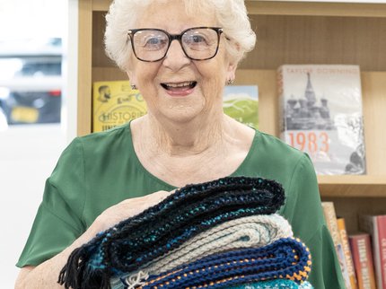 An elderly lady holds a pile of knitted scarves