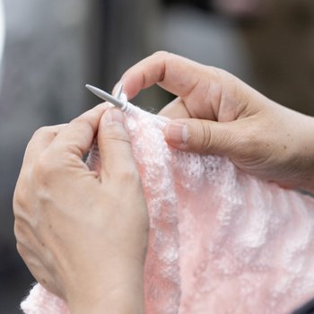 Hands knitting a pink scarf with knitting needles