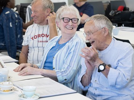 Three people sat in a line laughing and drinking tea
