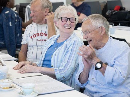 An elderly woman smiles at a table with other people sat around
