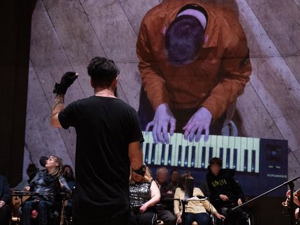 A man (Kris Halpin) playing the Miu Miu gloves with his back to the camera. A projection behind him of a man (Bradley) playing the keyboard.