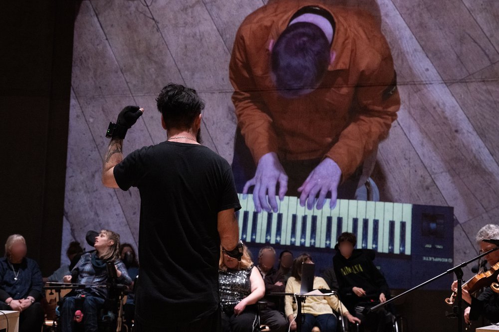 A man (Kris Halpin) playing the Miu Miu gloves with his back to the camera. A projection behind him of a man (Bradley) playing the keyboard.