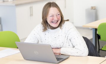 Adult learner smiling sat at a laptop.