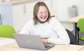 A woman with blonde hair sat in front of a laptop smiling